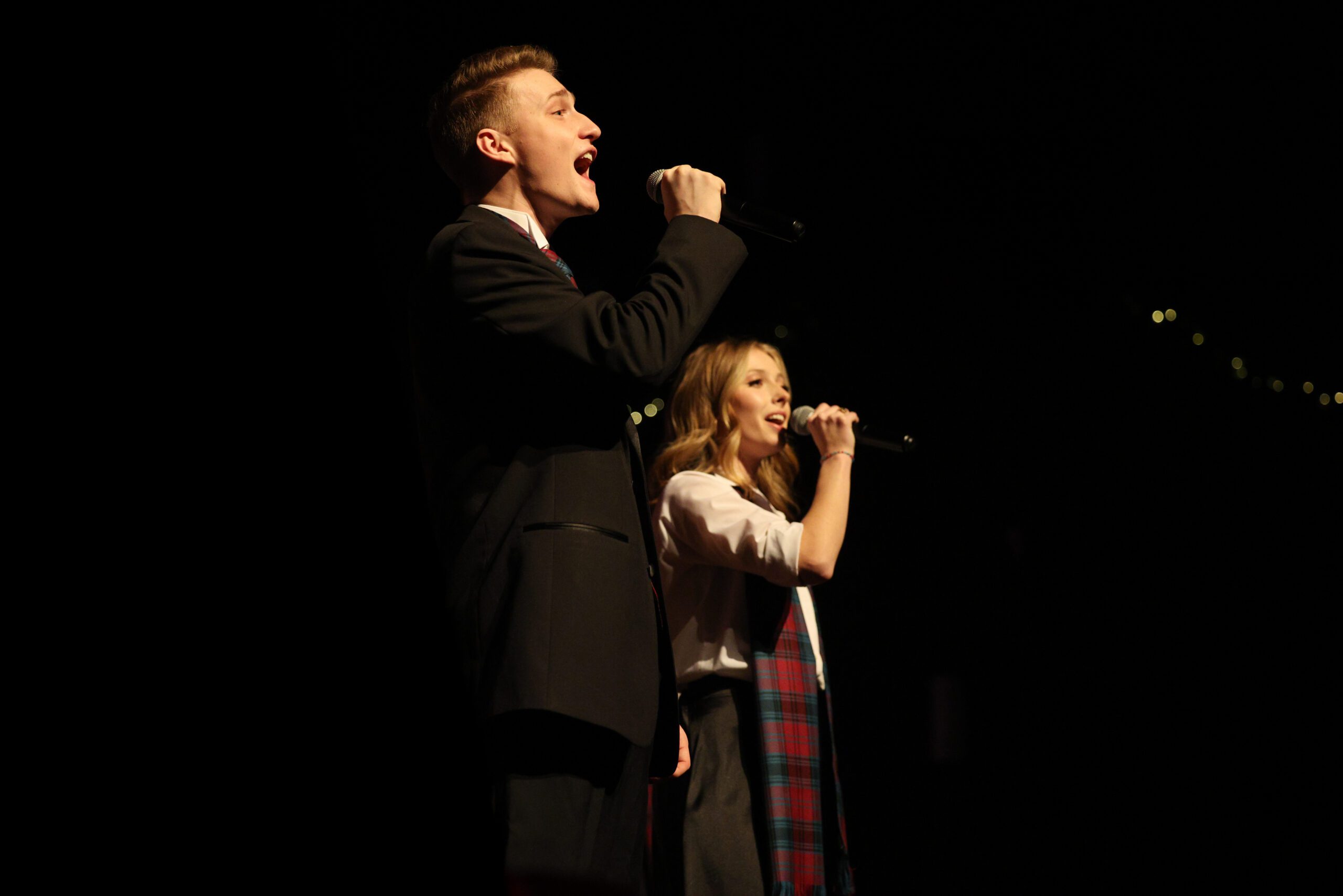 2 Alma College Students dressed up for the festival of carols singing with microphones. 