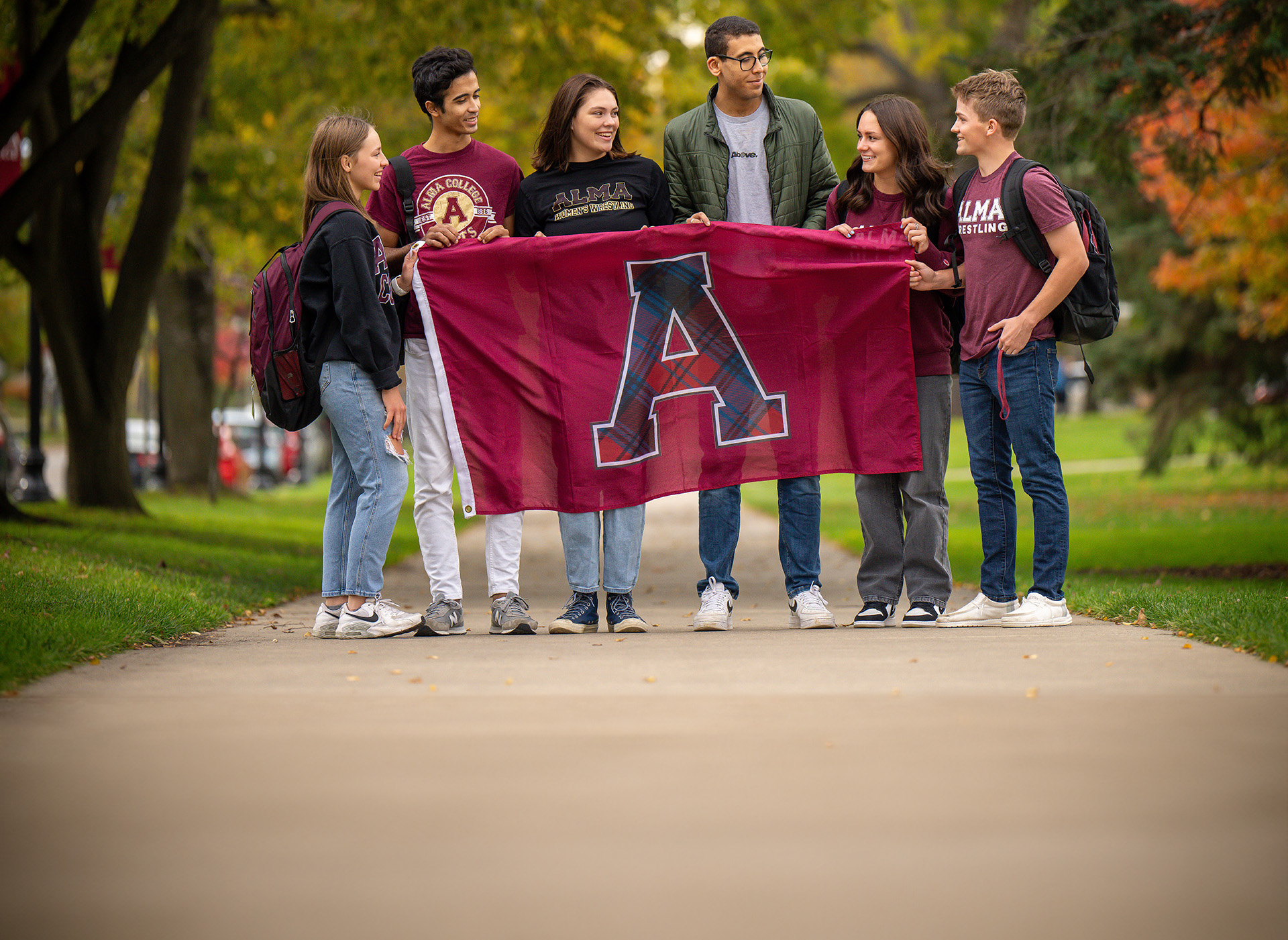 Students with Alma flag standing on the sidewalk and talking.