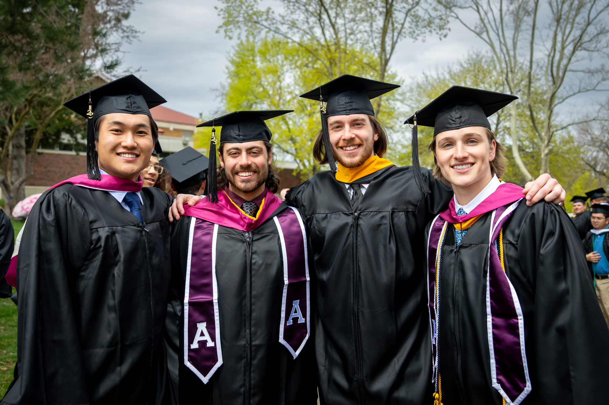 Group of four students wearing their graduation cap and gowns taking a photo at commencement.