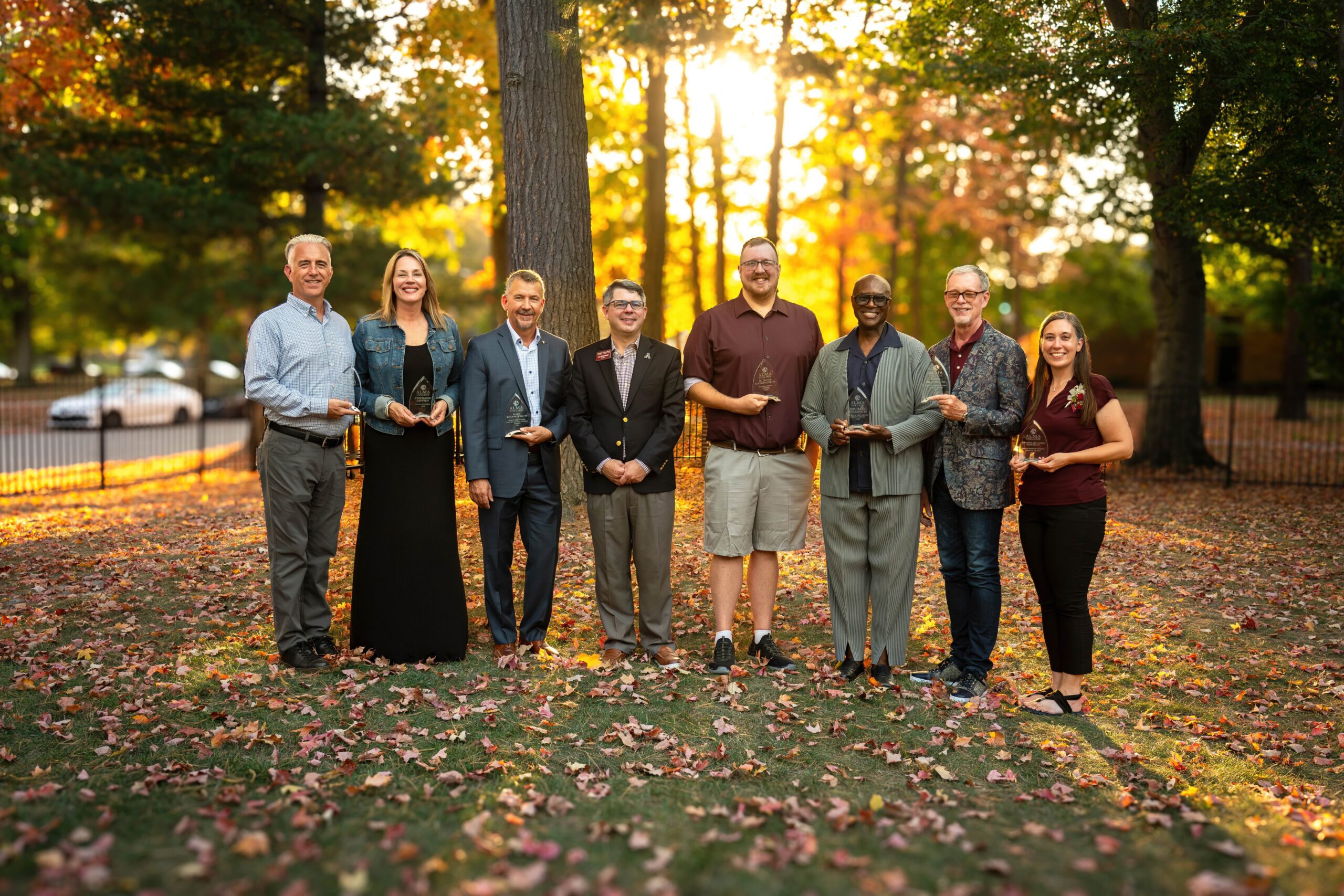 Group of 8 people holding alumni awards in the backyard of the Tracy house with President Joe