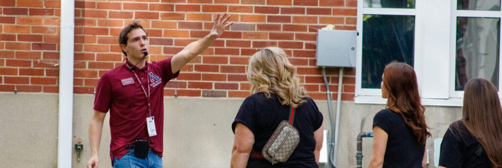 Student tour guide with mic on his head walking the campus while giving a tour to a group of people