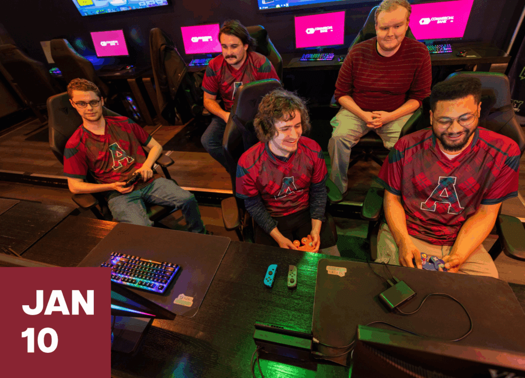 alma college's esports team gathered around a computer, laughing and having a great time
