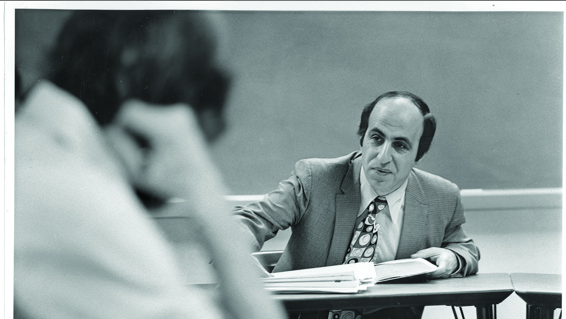 In this vintage photo, a middle-aged, male college professor in the background instructs a student in the foreground.