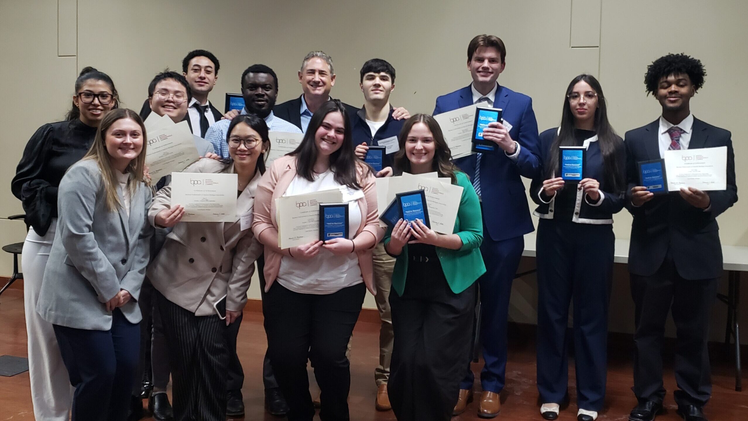 A group of 13 professionally dressed students are pictured posing with certificates they received as part of a group Business Professional of America competition.