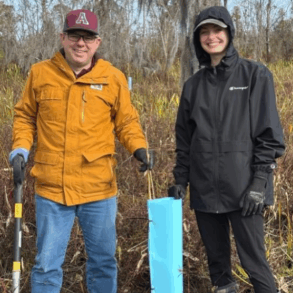 President Odenwald stands in a brush filled field planting trees with an Alma College student.