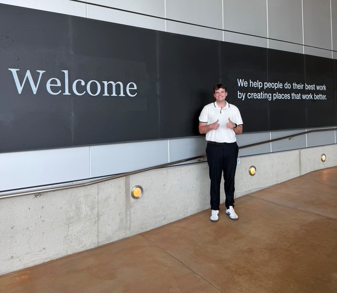 An Alma College students stands infront of a sign with a mission statement on it.