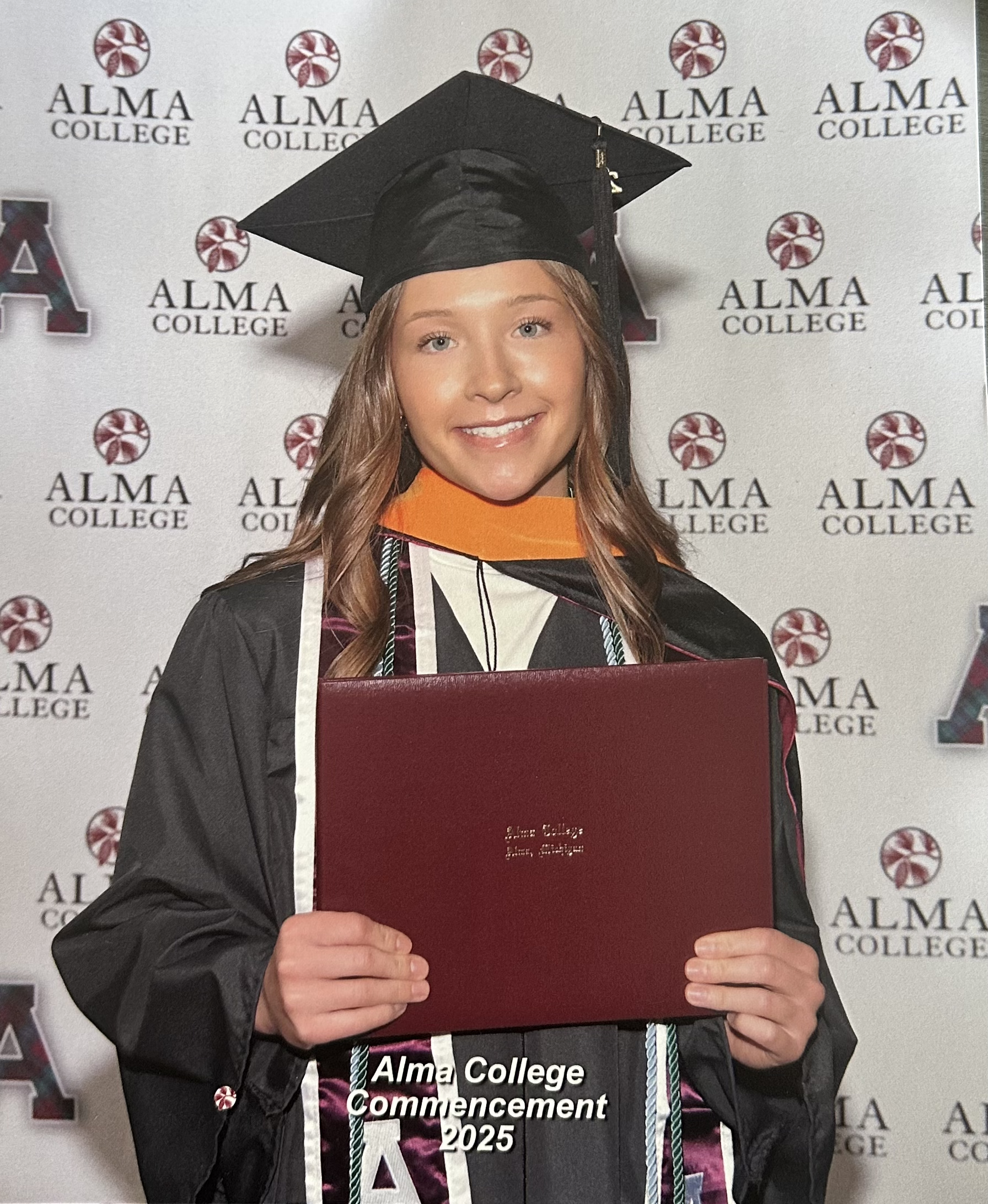 An Alma College students holds her diploma in her regalia.