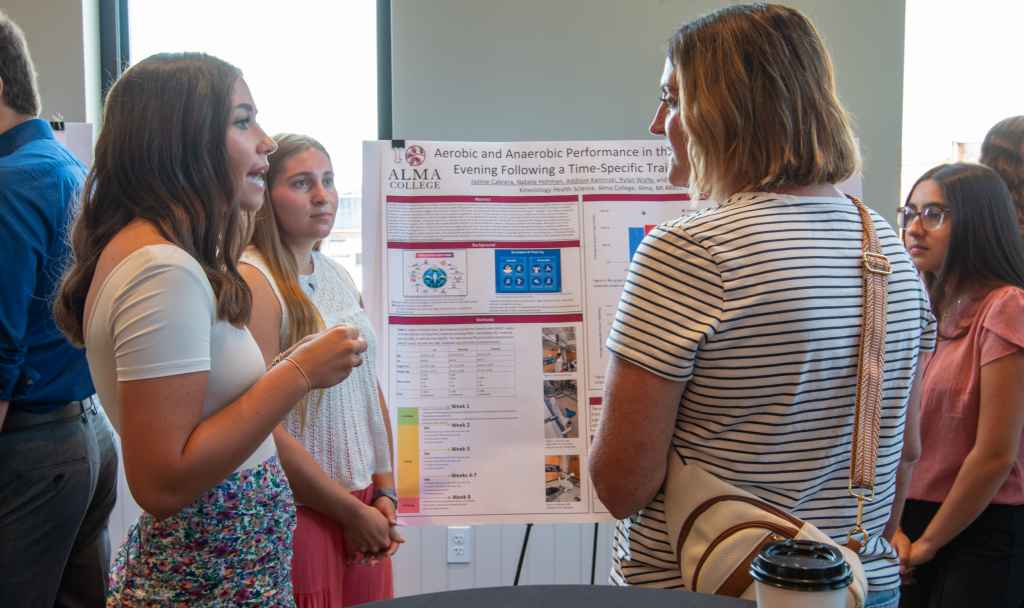Students presenting a poster presentation. 4 students stand in front of a poster displaying their research.