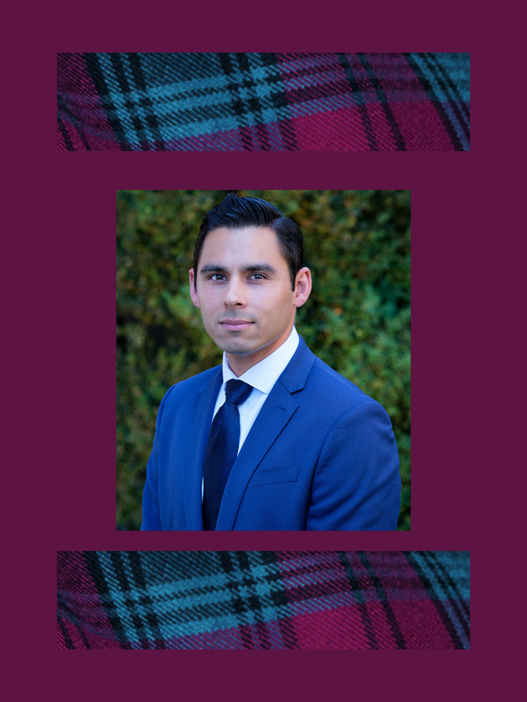 A man in a blue suit and tie poses outdoors in front of greenery, framed by a purple background with patterned fabric strips at the top and bottom.