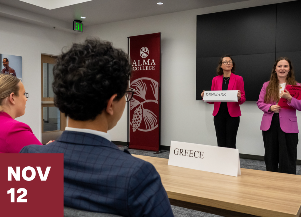 Four students participate in a mock conference at Alma College, offering a unique connect-and-visit experience. Two stand, holding signs for Denmark and another country; two are seated, with a Greece sign on the table. The date, Nov 12, is shown in the corner.