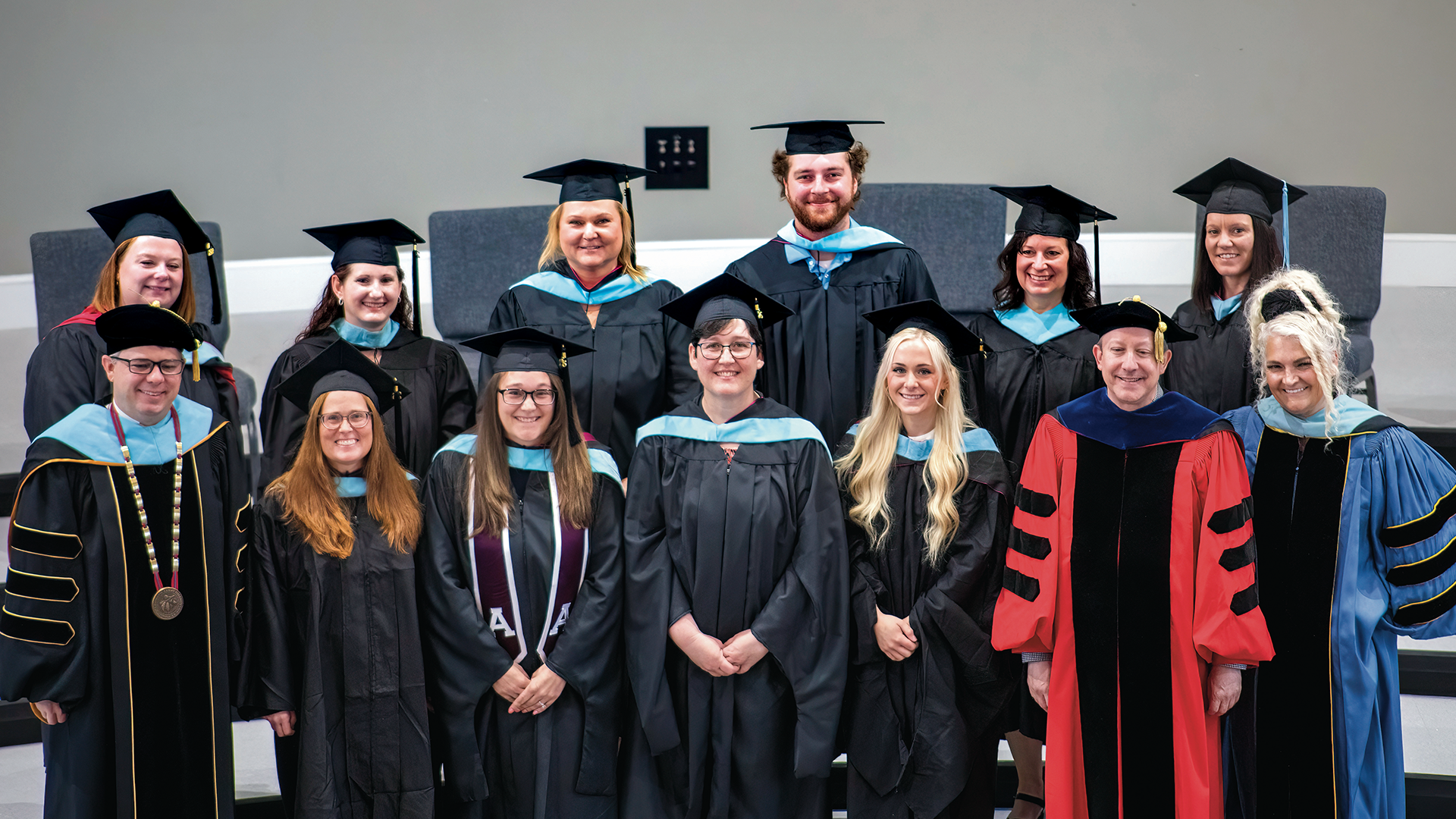 Thirteen graduates and faculty members in academic regalia posing for a photo to mark the transition from graduate study to real-world impact.