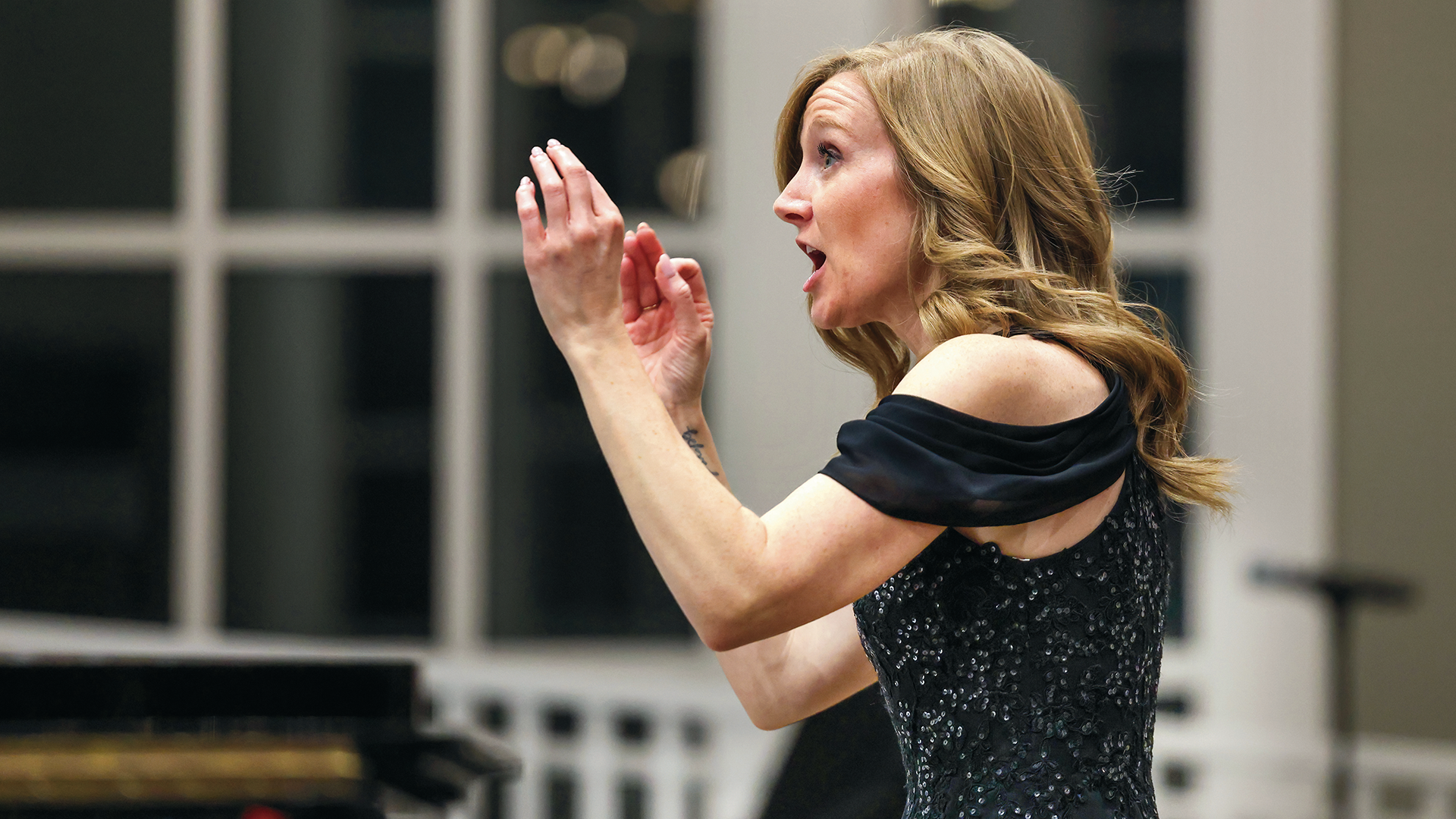 A female conductor leading the Alma Choir with expressive hand gestures and an open mouth.